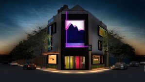 A modern building with a large illuminated display on the front, a parking lot, and a street view. - Ipanema Beach Hostel (Rio de Janeiro)