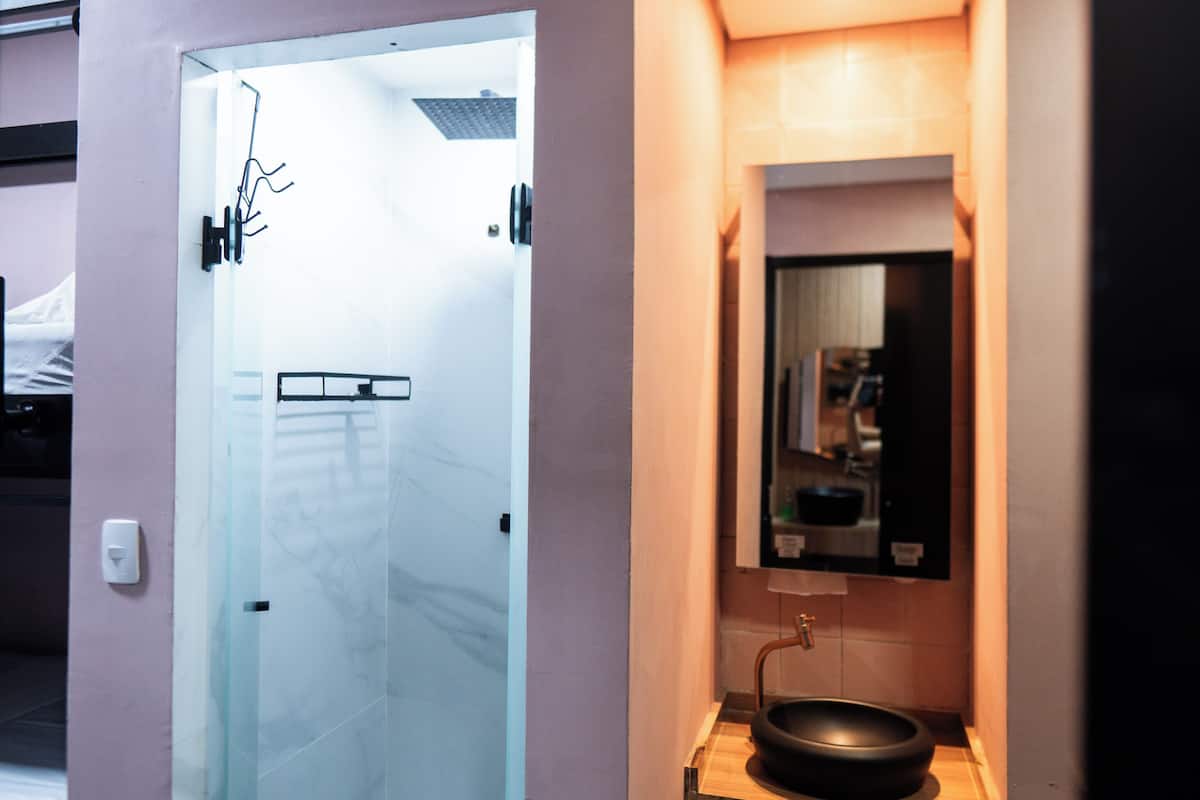 Un baño moderno con cabina de ducha de vidrio, un lavamanos negro y un espejo sobre él.