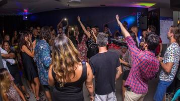 A crowded indoor event with people dancing and raising their hands, likely at a party or celebration.