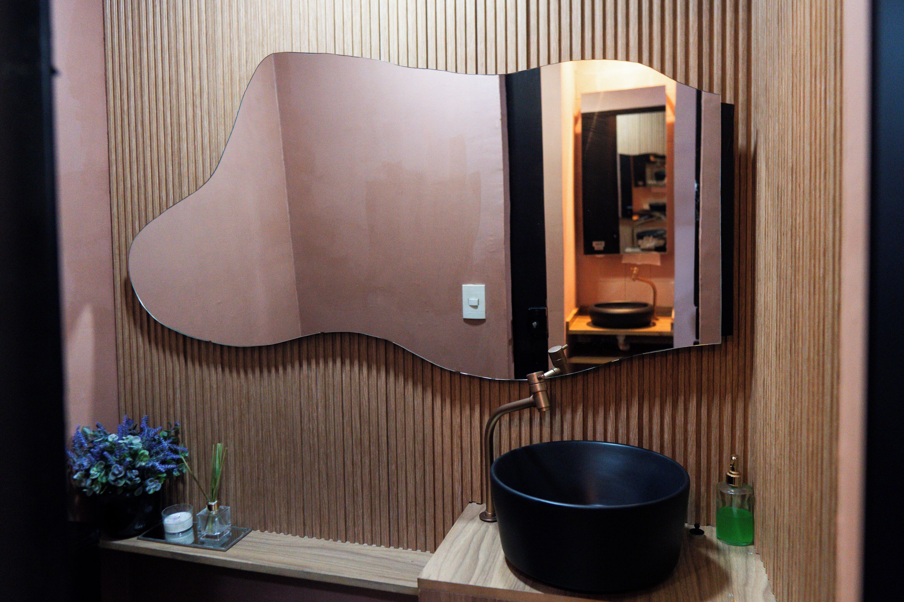 Une salle de bain dotée d’un miroir incurvé original, d’un lavabo noir et d’un meuble-lavabo en bois.