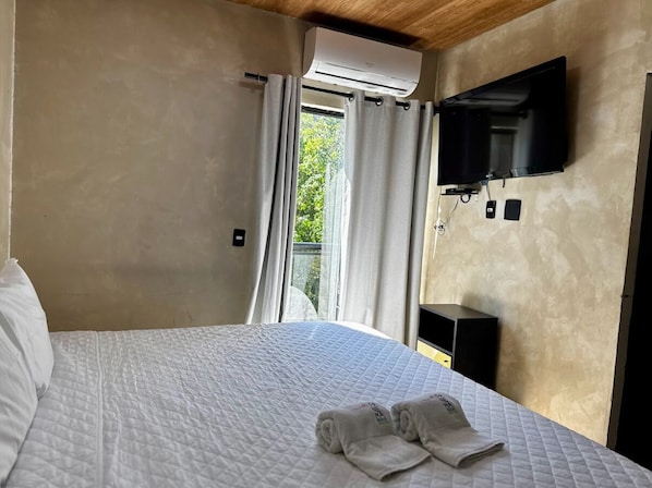 Un dormitorio con cama, televisor montado en la pared y ventana con cortinas.