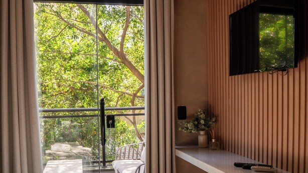 A modern room with a bed, a desk, two chairs, a TV mounted on the wall, and a window with curtains. - Ipanema Beach Hostel (Rio de Janeiro)