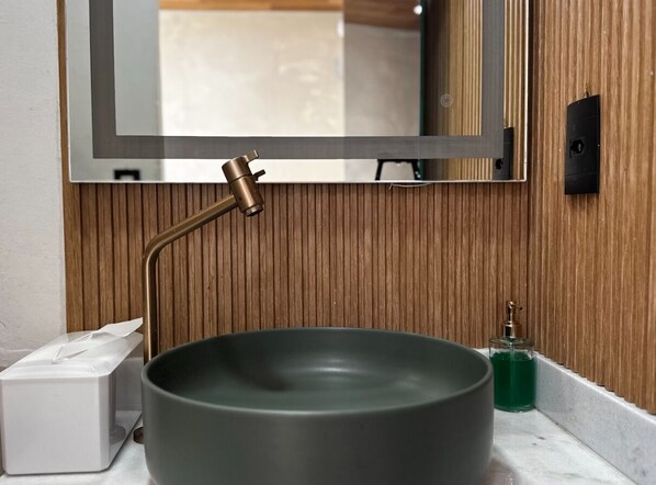 A bathroom with a wooden panel wall, a mirror, a modern sink with a faucet, a tissue box, and a soap dispenser.