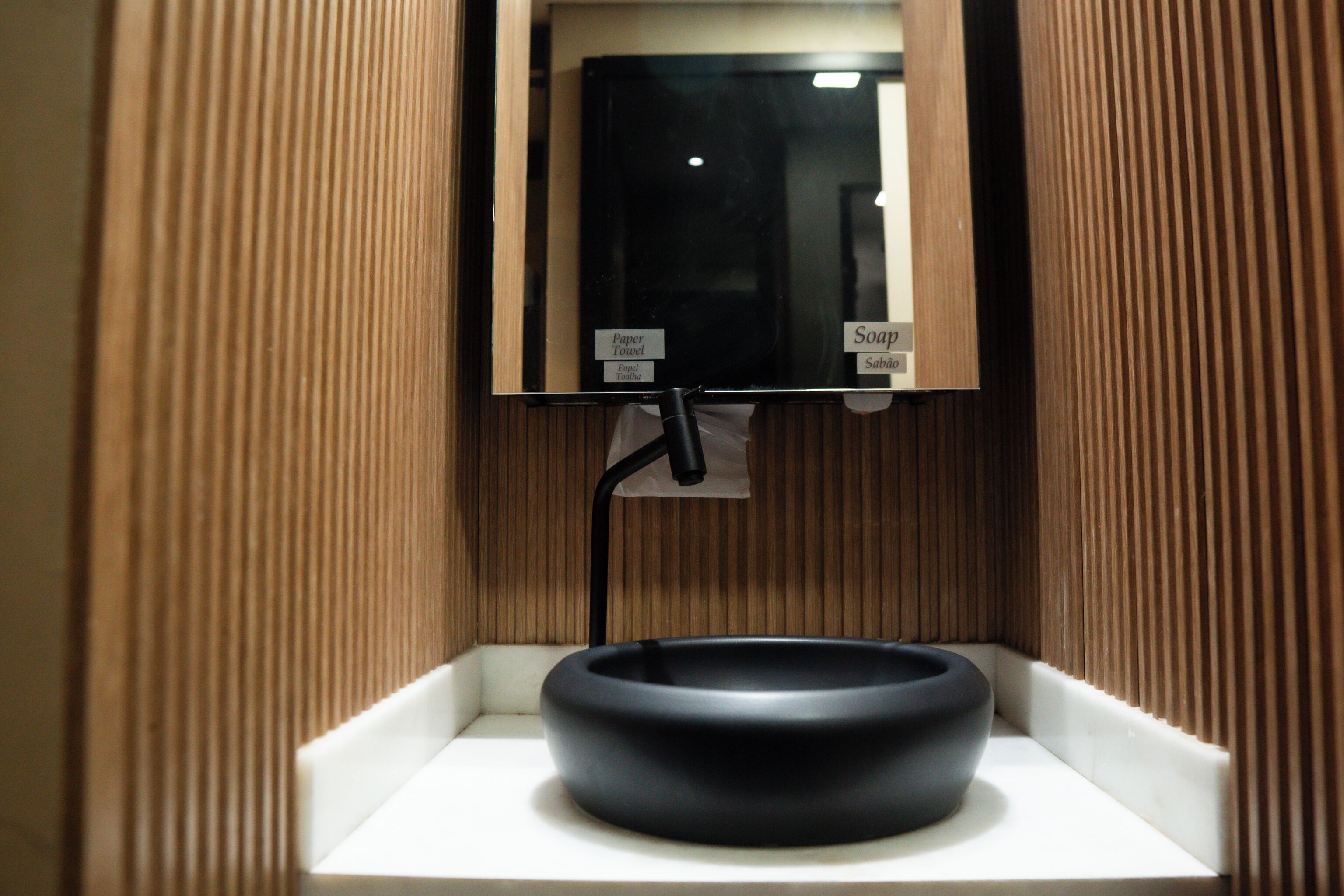 A bathroom with a black sink, a mirror, and a soap dispenser.