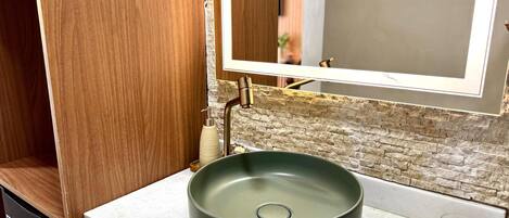 Un baño con un lavabo verde redondo, un espejo y una puerta de madera.