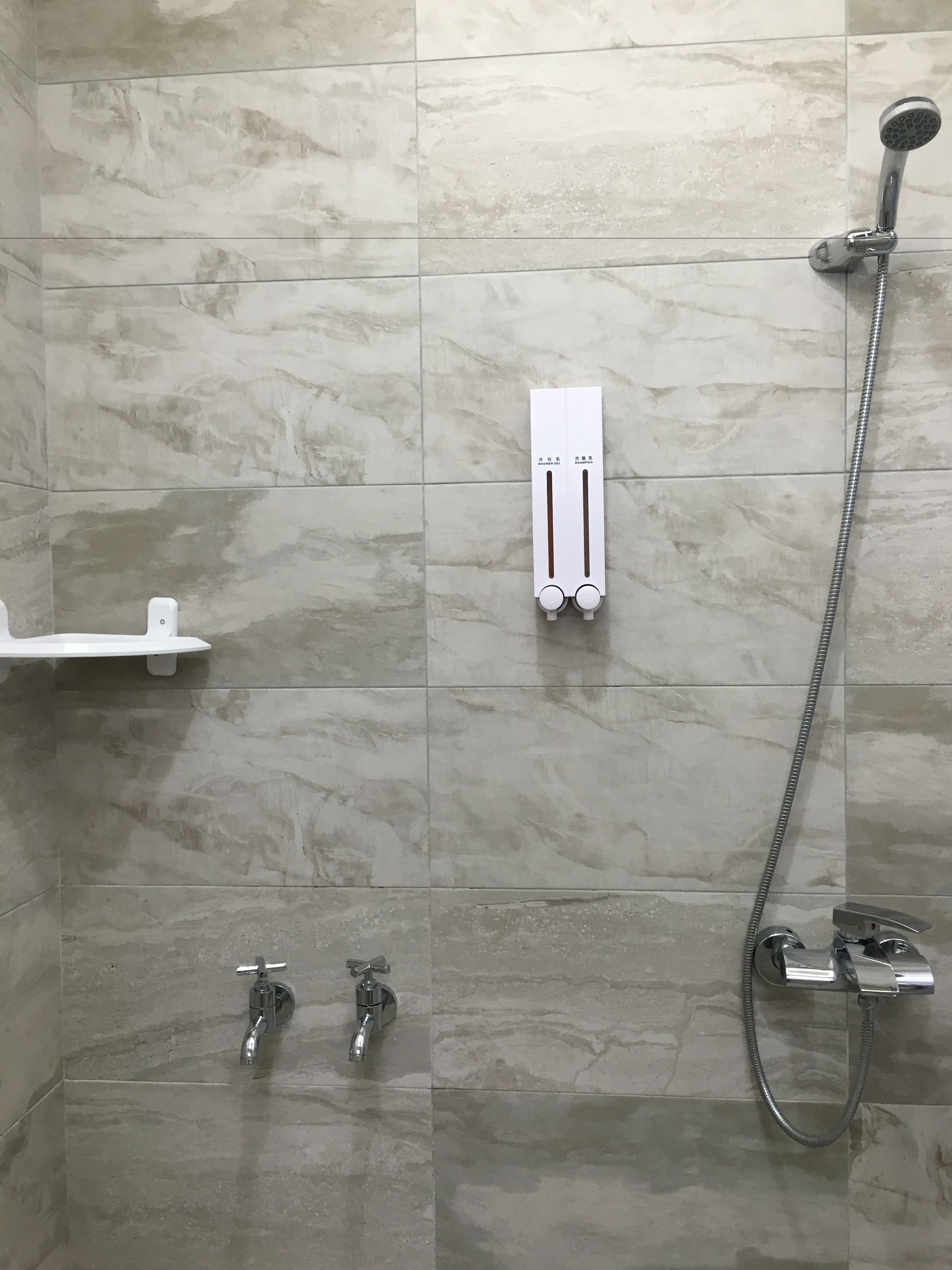 A bathroom with a shower, two faucets, and a shelf.