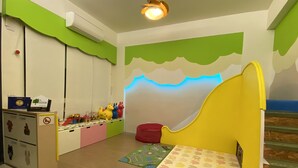 Quarto de criança com cama, espaço para brincar com brinquedos e escrivaninha com computador.