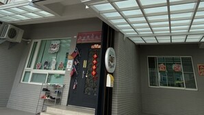 Um edifício moderno com cobertura de entrada em vidro, escadaria metálica que leva à entrada e uma placa com texto e imagens.