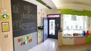 Uma sala de aula com cartazes educativos, um quadro-negro e uma janela com vista.