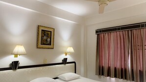 Een hotelkamer met een bed, twee bedlampen, een plafondventilator, een raam met gordijnen en een ingelijst kunstwerk aan de muur.