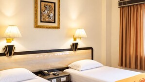 Ein Hotelzimmer mit zwei Betten, einem Nachttisch mit Telefon, einem gerahmten Bild an der Wand und einem Deckenventilator.