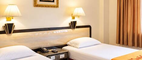 A hotel room with two beds, a nightstand with a phone, a framed picture on the wall, and a ceiling fan.