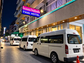Un hotel tailandés con varias camionetas blancas estacionadas frente, lo que sugiere una zona de servicios o transporte.