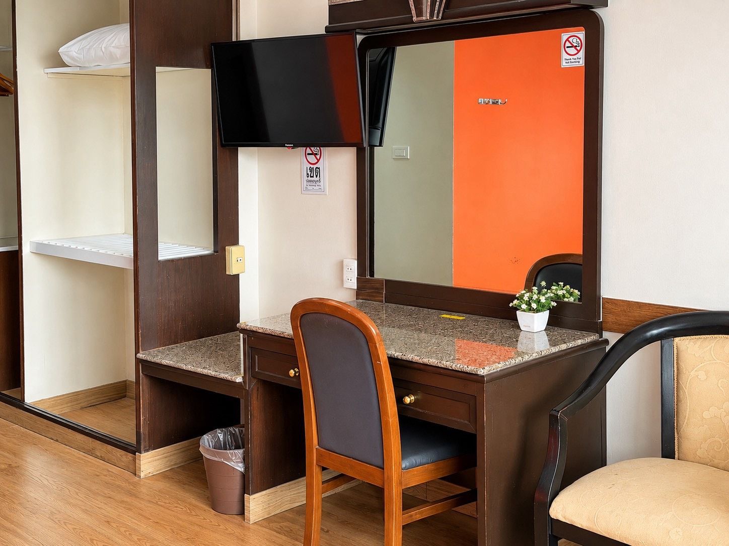 Ein Hotelzimmer mit Schreibtisch aus Holz, einem Sessel, einem Fernseher, einem Spiegel und einer kleinen Topfpflanze.