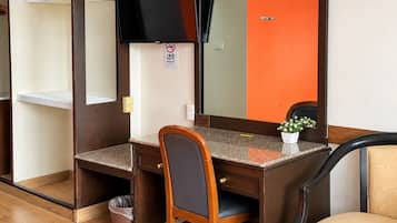 Habitación de hotel con escritorio de madera, una silla, televisor, espejo y una pequeña planta en maceta.