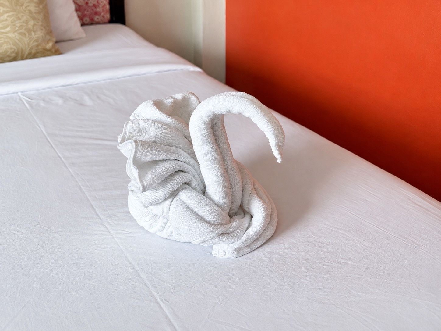 A bed with a white sheet and a towel shaped like a swan.