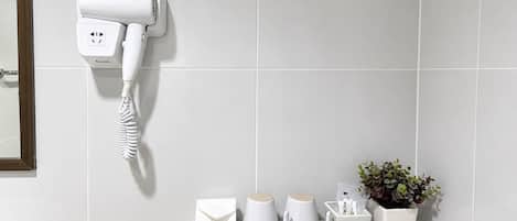 A bathroom with a white hairdryer mounted on the wall, a white shelf with toiletries, and a potted plant.