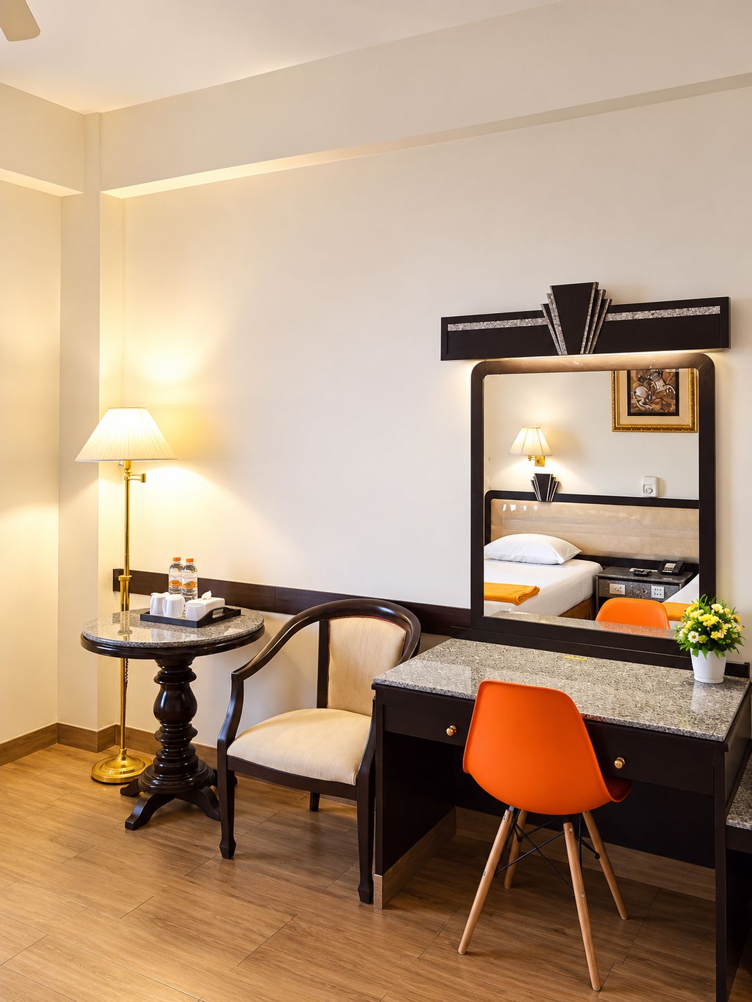 A hotel room with a bed, a desk, a chair, a lamp, and a mirror.
