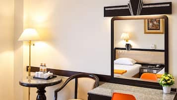 A hotel room with a bed, a desk, a chair, a lamp, and a mirror.