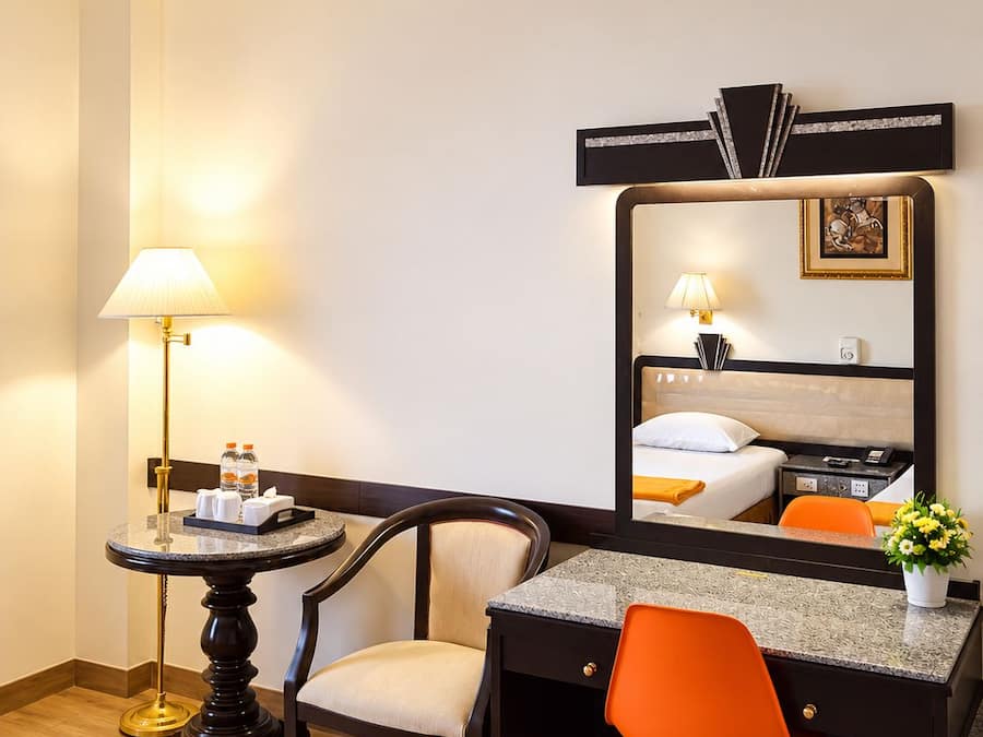 Una camera d'albergo con un letto, una scrivania, una sedia, una lampada e uno specchio.