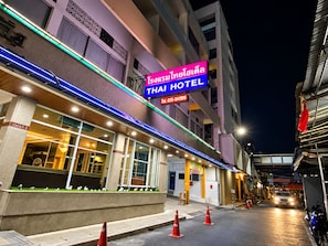 Un hôtel avec une enseigne au néon, une entrée bien visible et une vue sur la rue, avec des cônes de signalisation.