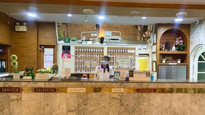 Een hotel receptie met een marmeren balie, borden met dienstverlening en receptie informatie, een kassa en een presentatie van toiletartikelen.