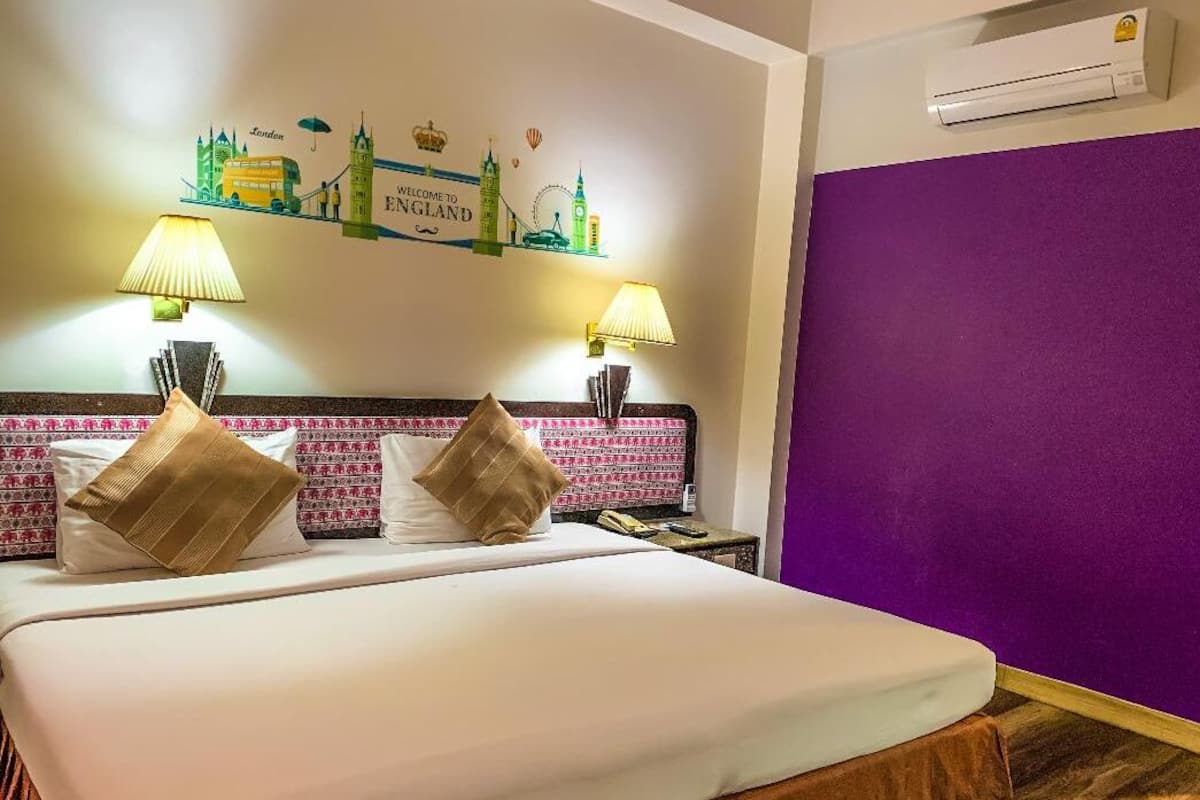 Een hotelkamer met een bed, twee lampen, een paarse muur en een welkomstbord.