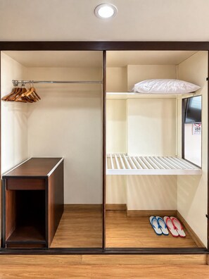 Una habitación con armario, un escritorio pequeño, una cama con colchón y almohadas, y un par de chanclas en el suelo.
