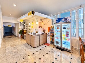 Een hotel lobby met een receptiebalie, een koelkast gevuld met drankjes, en een betegelde vloer.