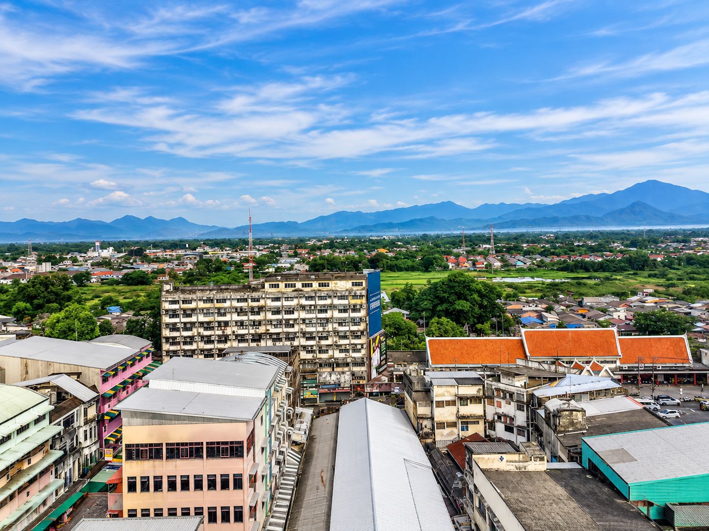 A cityscape with a mix of residential and commercial buildings, a prominent blue sign, and a mountainous backdrop.
