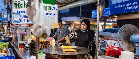 A street food vendor preparing food at a stall with a large cooking surface and various condiments.