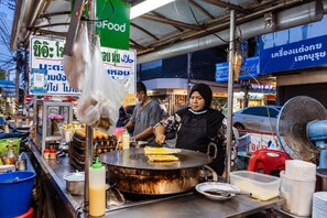 Un vendeur de nourriture de rue prépare des plats sur un stand équipé d’une grande surface de cuisson et de divers condiments.