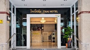 Der Eingang zum Thai Hotel mit einer Treppe, die zum Eingang führt, einer Glastür und einem Schild über der Tür.