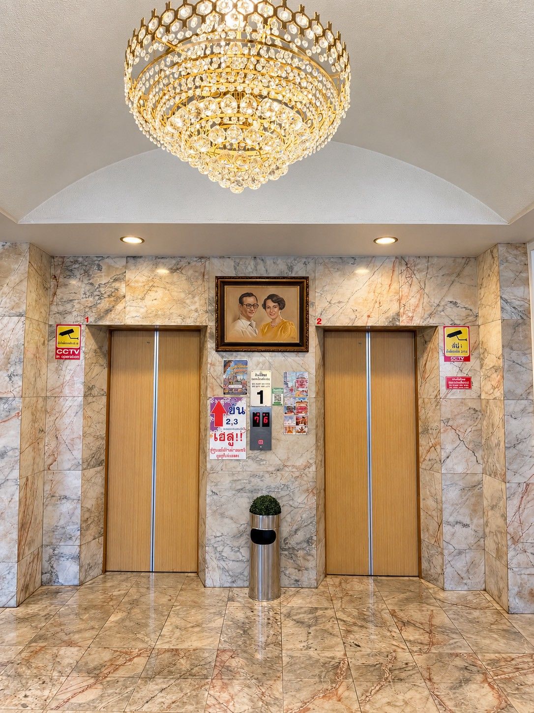 A lobby with marble flooring, two elevators, a chandelier, and a framed picture on the wall.