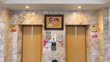 A lobby with marble flooring, two elevators, a chandelier, and a framed picture on the wall.