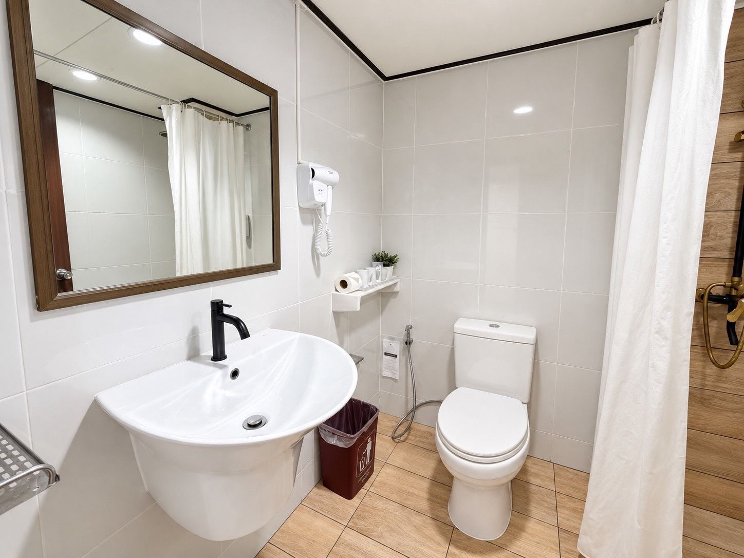 Une salle de bain avec un lavabo blanc, des toilettes, un espace douche et un miroir.