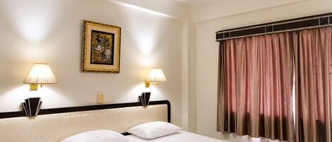 A hotel room with a bed, two bedside lamps, a ceiling fan, a framed picture on the wall, and a window with curtains.