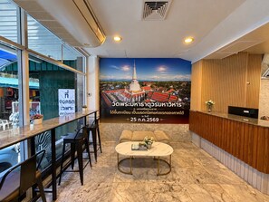 Een hotel lobby met een receptiebalie, een zithoek en een groot poster van een tempel.