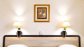 A hotel room with two beds, a ceiling fan, bedside lamps, a framed artwork on the wall, and a small table with a phone and magazines.