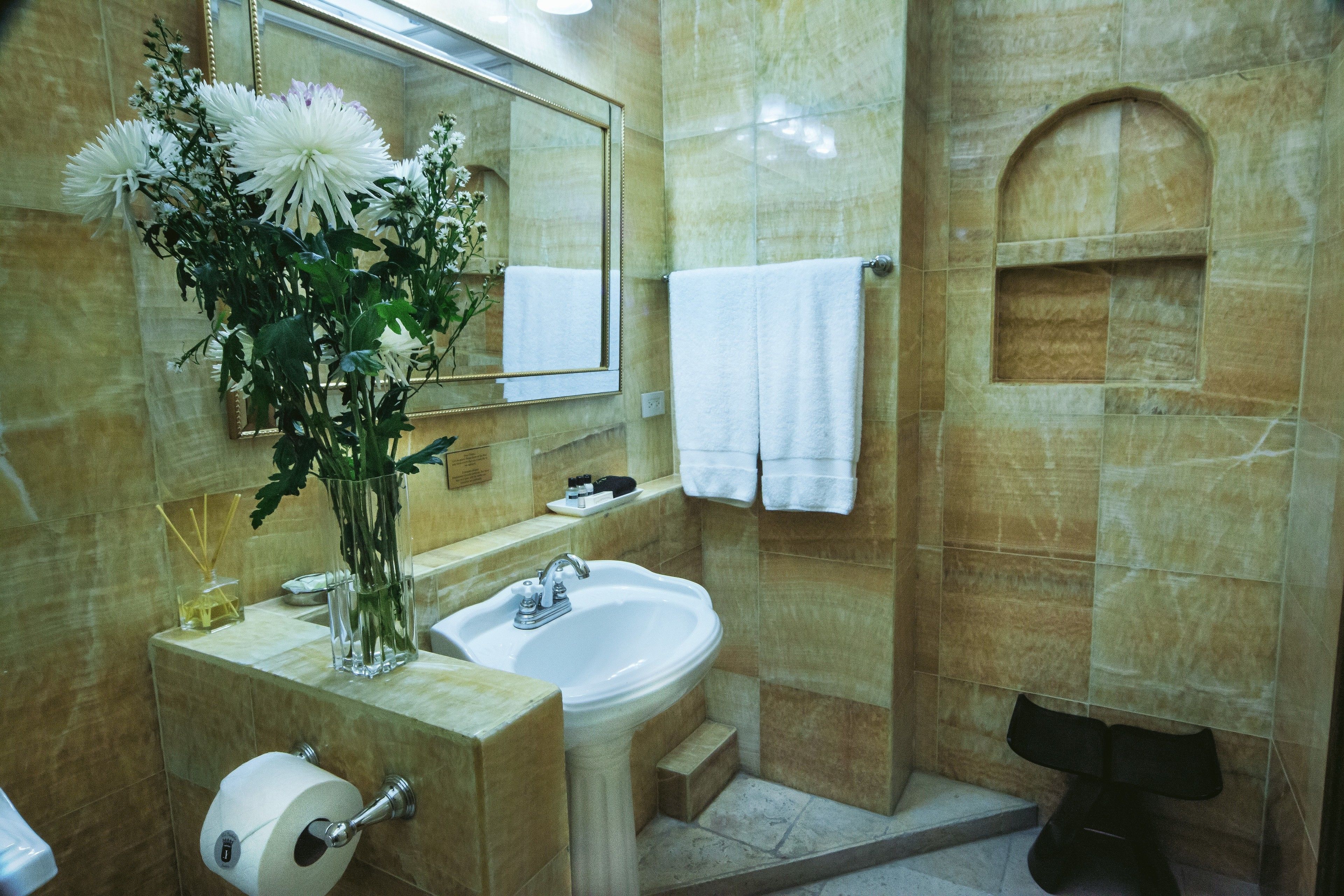 A bathroom with a sink, mirror, and a vase of flowers.
