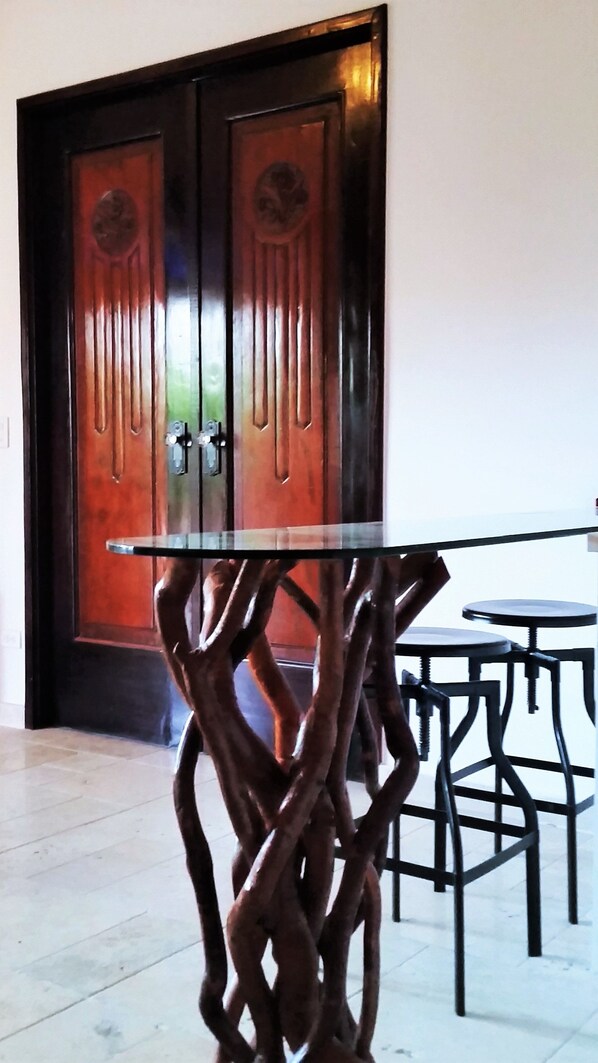 A modern interior with a glass-top table and twisted metal legs, a wooden door with vertical panels, and a tiled floor. - La Isabela Suites (Panama City)