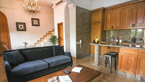 A living room with a sofa, a coffee table with books, a chandelier, and a kitchen with wooden cabinets and granite countertops. - La Isabela Suites (Panama City)