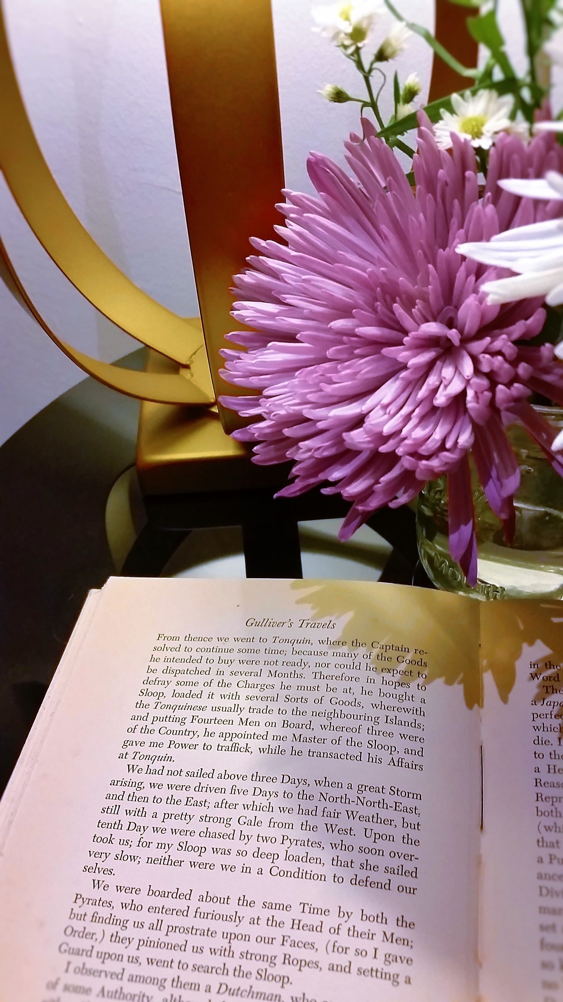 An open book titled 'Gulliver's Travels' with a pink flower in a vase on a table.