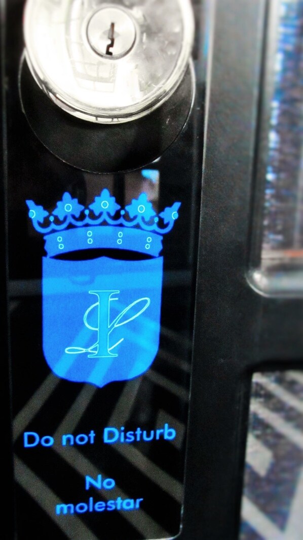 A close-up of a door handle with a blue emblem and the text "Do not Disturb No molestar" on a black surface. - La Isabela Suites (Panama City)