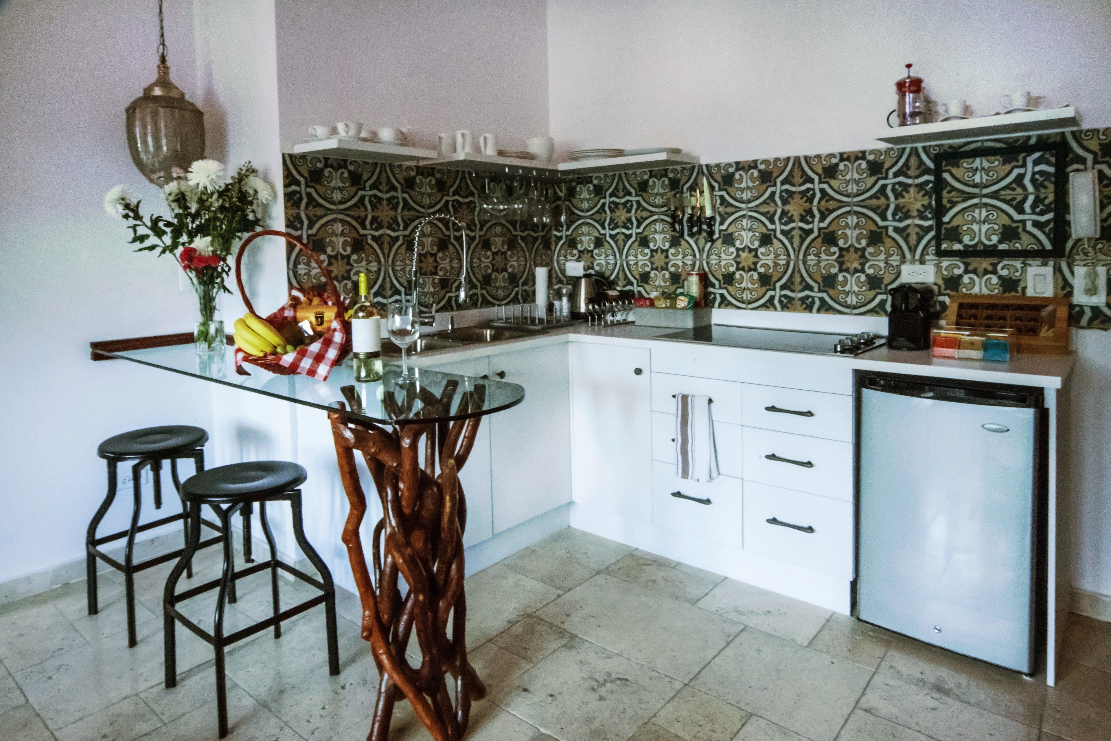 Una cocina con una isla de vidrio, taburetes de bar, un refrigerador y un salpicadero con diseño.