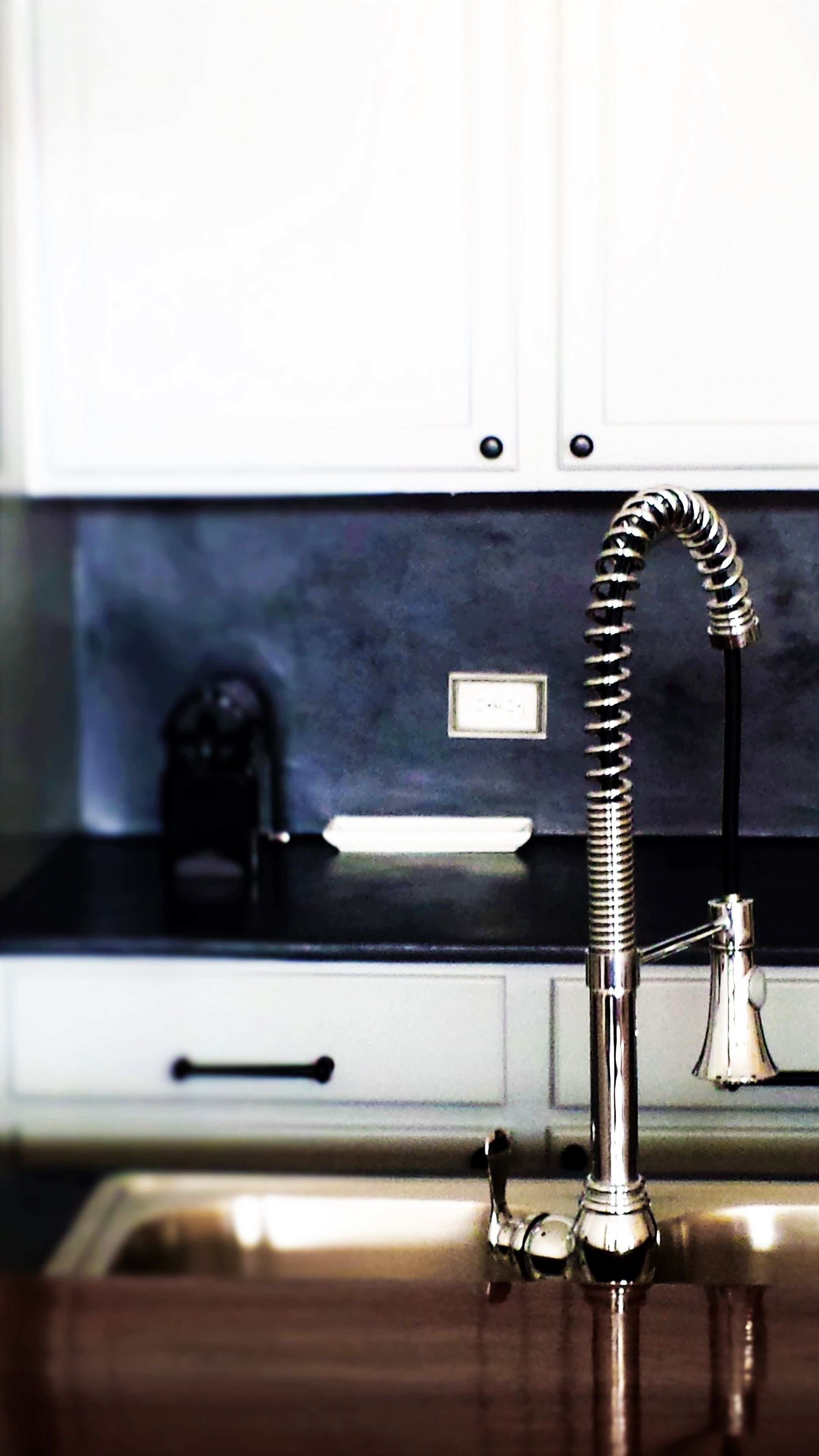 A kitchen with a stainless steel faucet, a black countertop, and white cabinets.