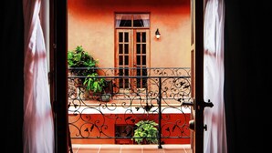 An open door revealing a balcony with a wrought iron railing, potted plants, and a window with a curtain. - La Isabela Suites (Panama City)