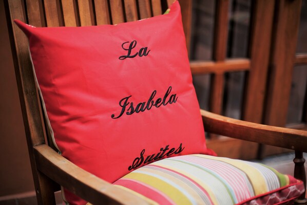 A red pillow with "La Isabela Suites" embroidered on it, placed on a wooden chair with a colorful striped cushion. - La Isabela Suites (Panama City)