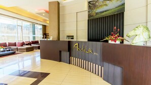 A hotel reception area with a modern design, featuring a reception desk, a large window, and a seating area with sofas. - Andelir Hotel (Bandung)