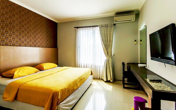 A hotel room with a bed, a TV, an air conditioner, and a window with curtains. - Andelir Hotel (Bandung)